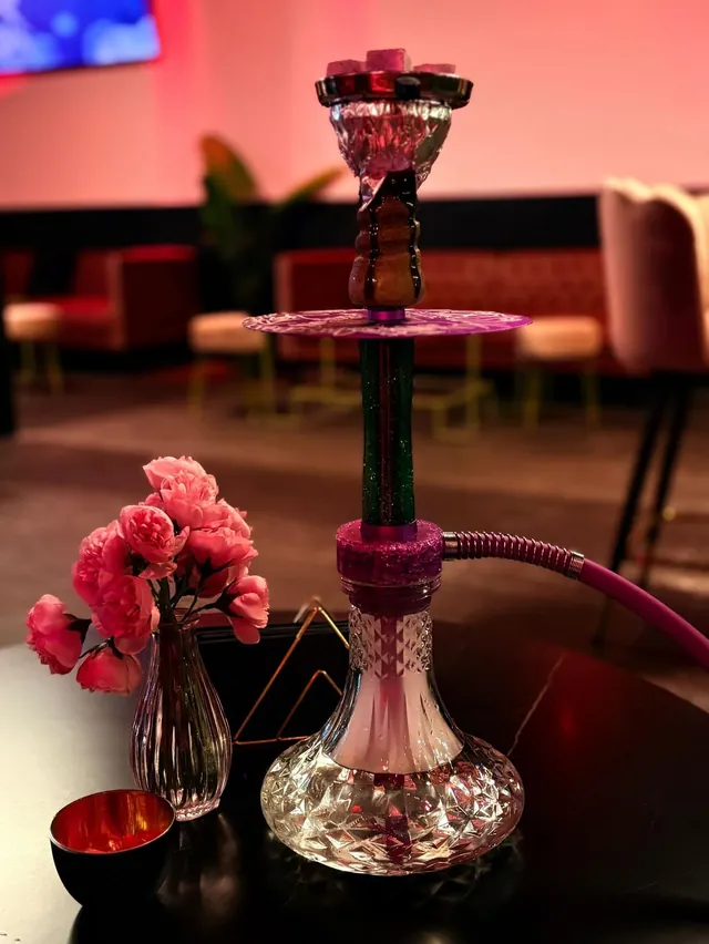 Cachimba con base de cristal y un jarrón de flores rosas sobre la mesa