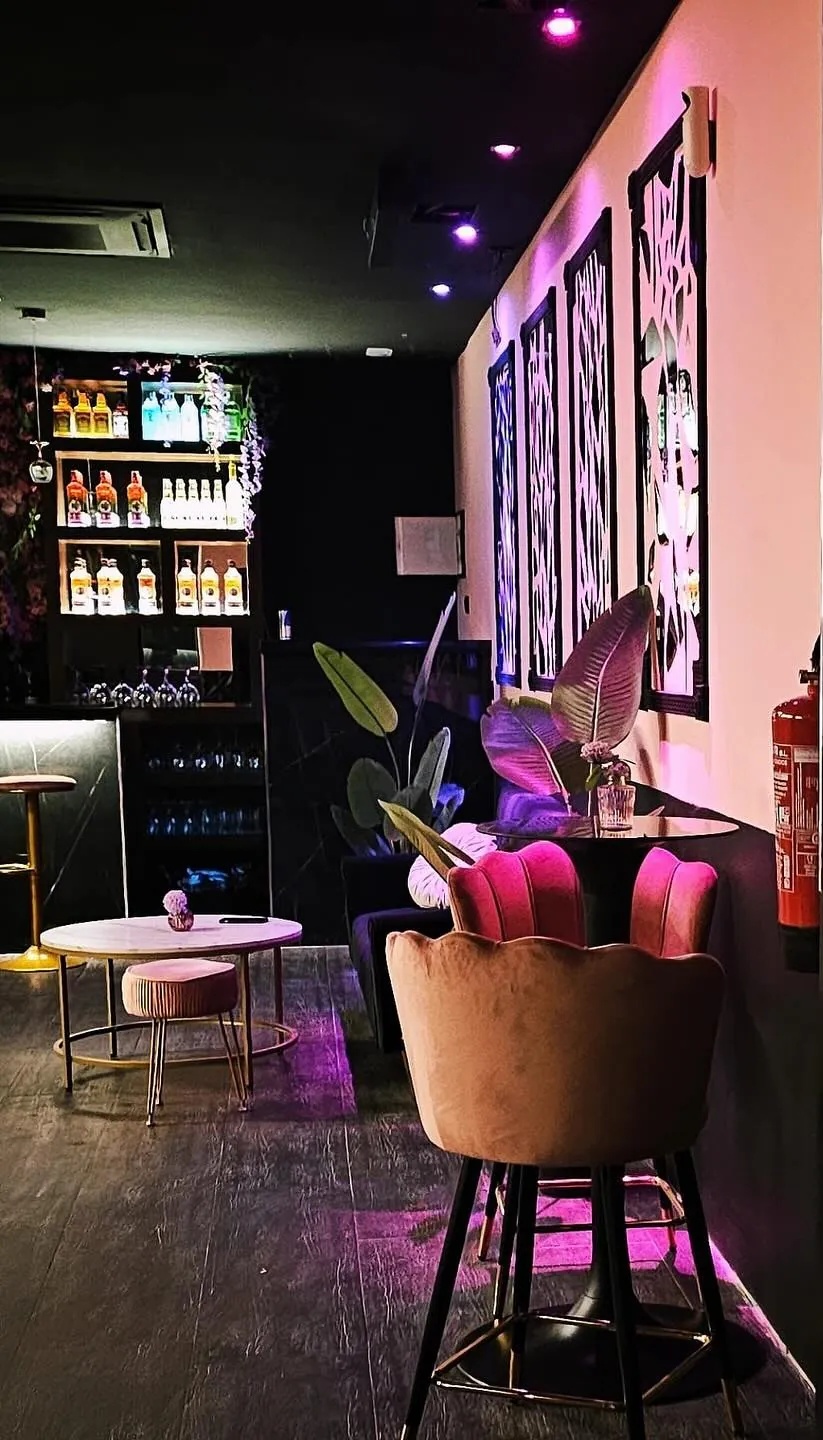 Rincón de Capricho con una silla rosa, una mesa baja y la barra con botellas